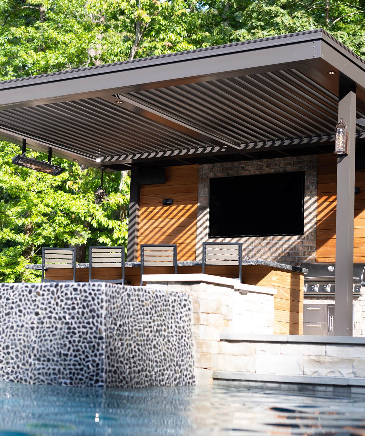 Poolside outdoor kitchen covered by a modern louvered shade structure